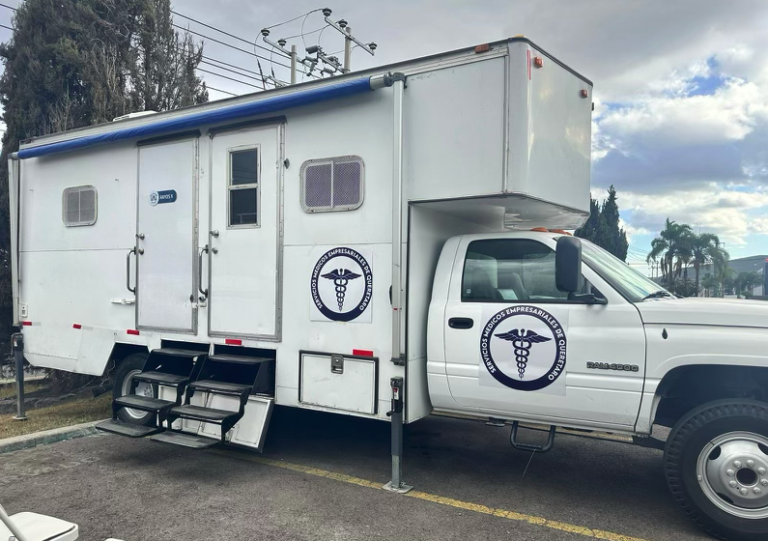 Interior de una ambulancia equipada con equipo médico y una camilla, con la puerta abierta que revela el diseño organizado, incluyendo compartimentos de almacenamiento con suministros médicos, un asiento para un profesional médico y una camilla lista para el transporte de pacientes, para la sección Ambulancias y Unidades Médicas Móviles de Salud Empresarial de México.